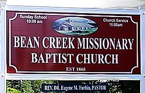 Maroon church sign reading Bean Creek Missionary Baptist Church, Sunday School 10:00 am, Church Service 11:00 am, Rev. Dr. Eugene M. Harbin, Pastor.