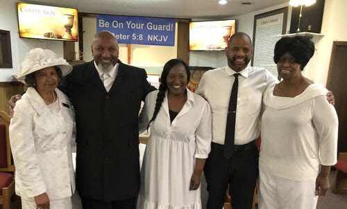 Five members of the congregation standing together in the sanctuary, dressed in white, under a blue banner that reads Be On Your Guard, 1 Peter 5:8.