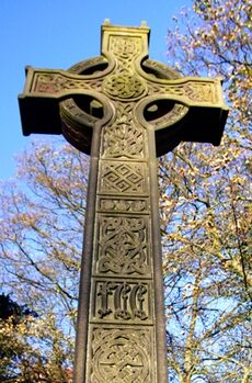 A carved stone Celtic cross against a blue sky.