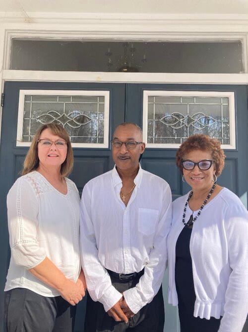 Three church members smiling in front of the blue church doors.