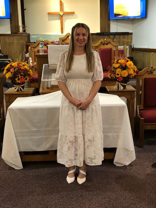 Deaconess Britny Trammell in a white dress stands in front of the communion table.
