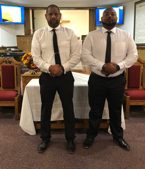 Deacons Rickey Johnson and Chase Trammell stand in front of the communion table.