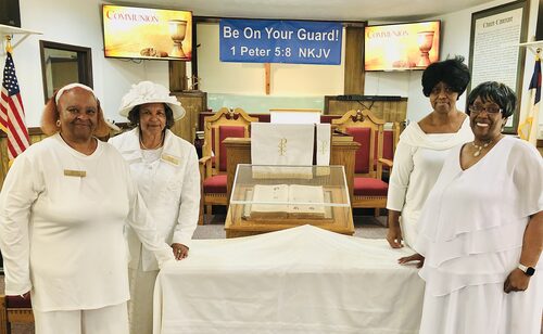The Mother Board, women dressed in white, stand behind the communion table.