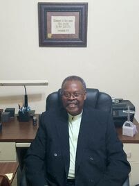 Reverend Dr. Eugene M. Harbin seated at his desk in the pastor's study, smiling.