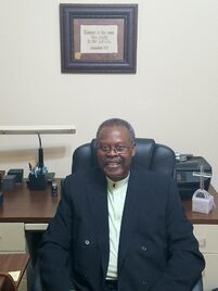 Reverend Dr. Eugene M. Harbin seated at his desk in the pastor's study, smiling.