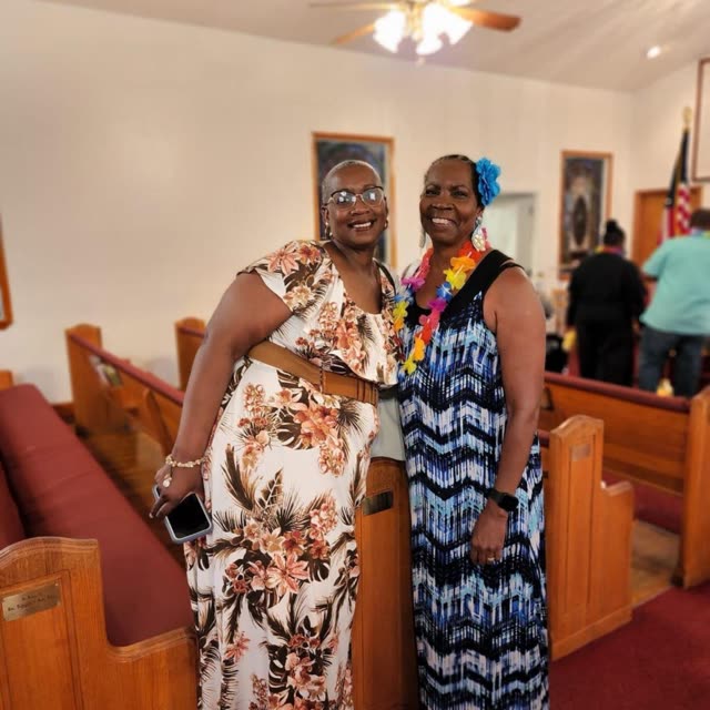 Two women in long patterned dresses stand among the pews.