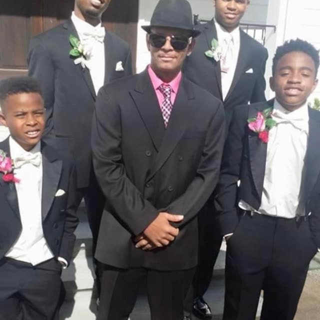 Young men and boys in dark suits pose together.