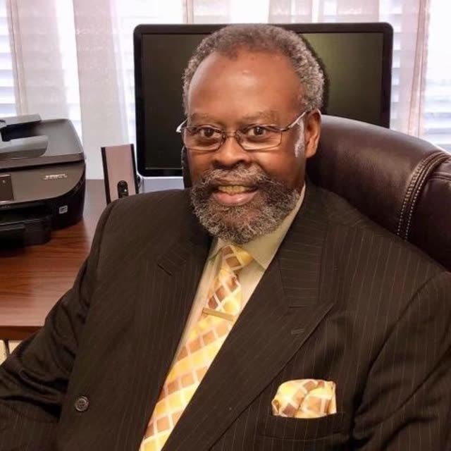 A man in a suit and tie sits at a desk.