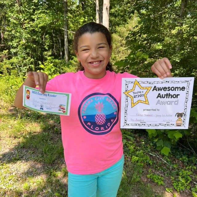 A girl in a pink shirt holds up an Awesome Author certificate outdoors.