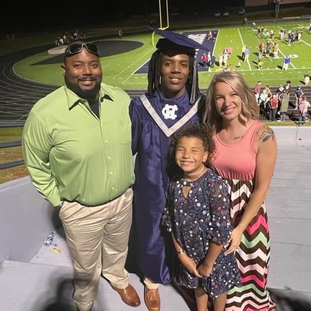 A family stands with a graduate in a cap and gown on a football field.