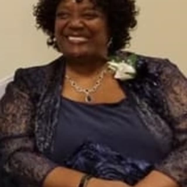 A smiling woman in a dark top with a corsage.