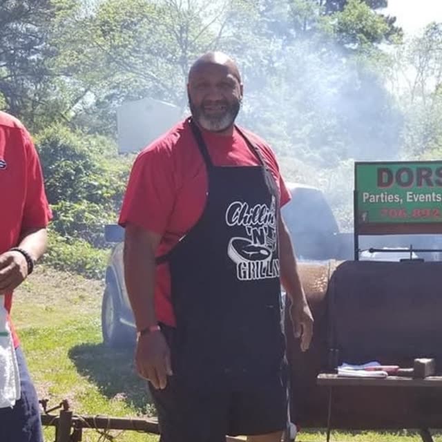 A man in a red shirt and an apron stands outdoors.