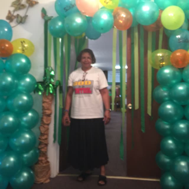 A woman stands under an arch of green and white balloons.