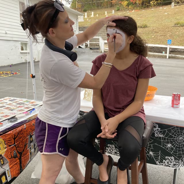 A woman paints a girl's face at an outdoor event.
