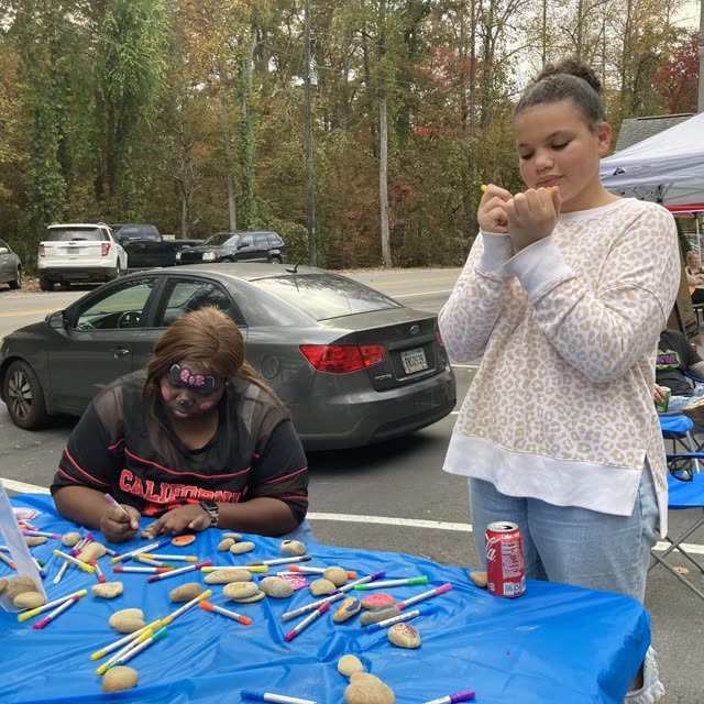 A girl stands by a table with a blue cloth at an outdoor event.