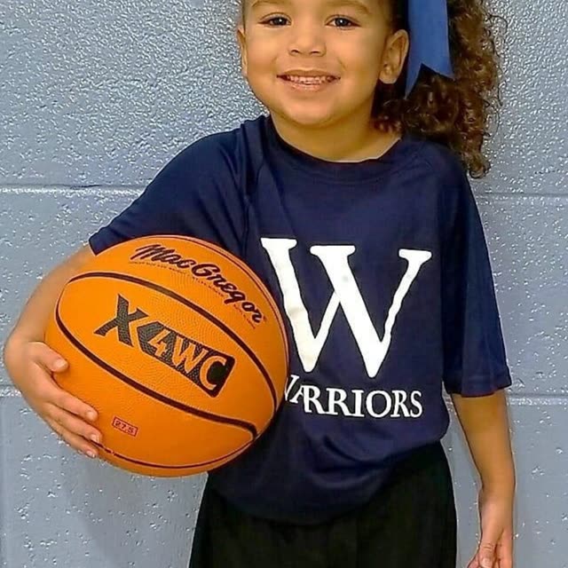A girl in a Warriors jersey holds a basketball.