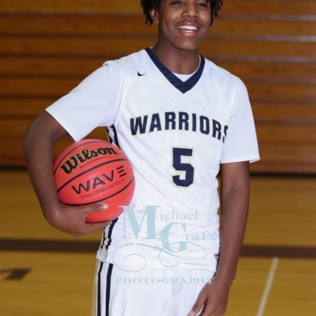 A young man in a white Warriors number 5 jersey holds a basketball.