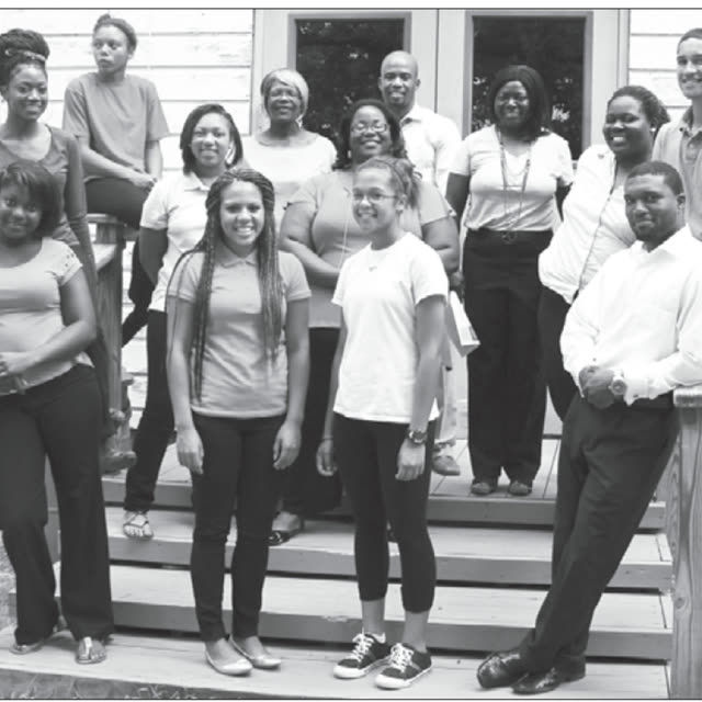 A black and white photo of a group standing on a porch and its steps.