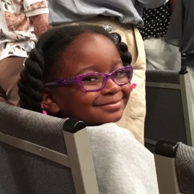 A girl with purple glasses smiles in a pew.