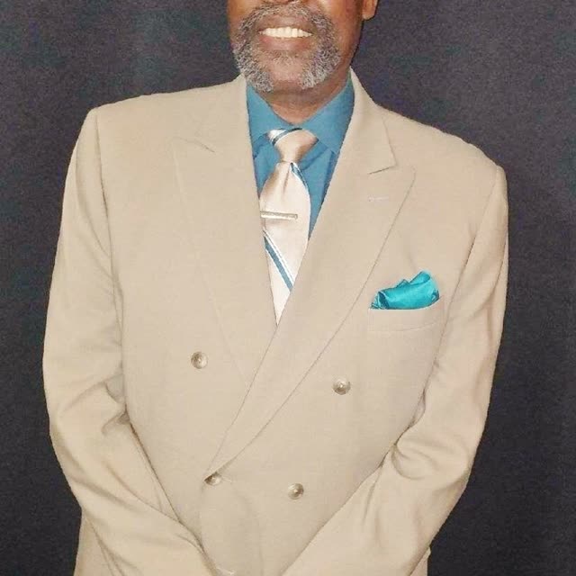 A man in a cream suit and a blue shirt.