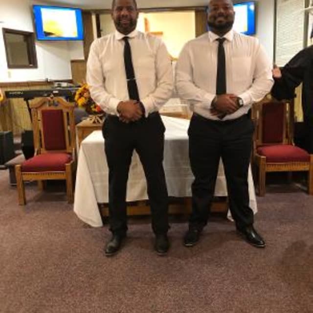 Two deacons in white shirts and ties stand in front of the communion table.