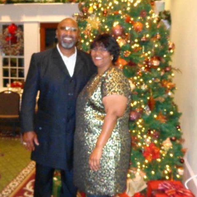 A man and a woman stand by a decorated Christmas tree.