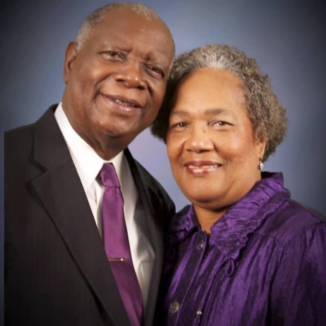 An older man in a suit and an older woman in purple.