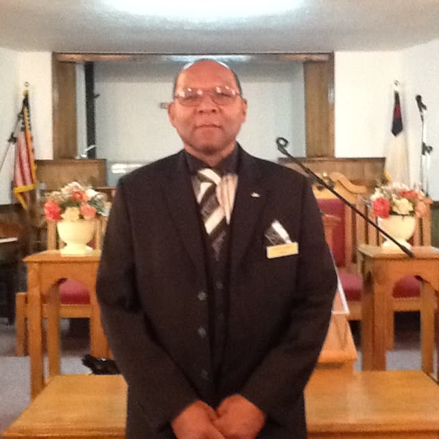 A man in a dark suit stands at the front of the sanctuary.