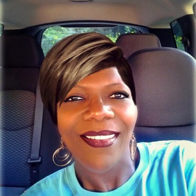 A smiling woman takes a selfie in a car.