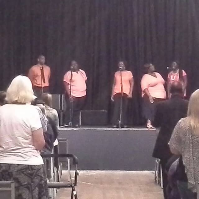 A choir in pink tops sings on a stage.