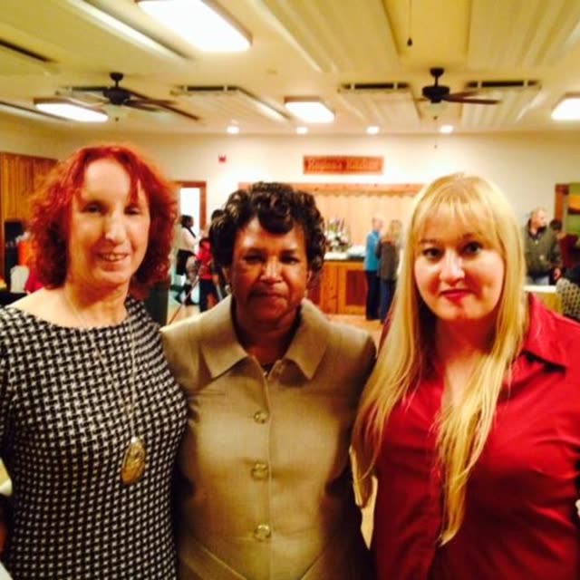 Three women smile together indoors.