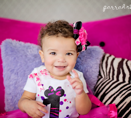 A smiling baby sits on a pink chair.