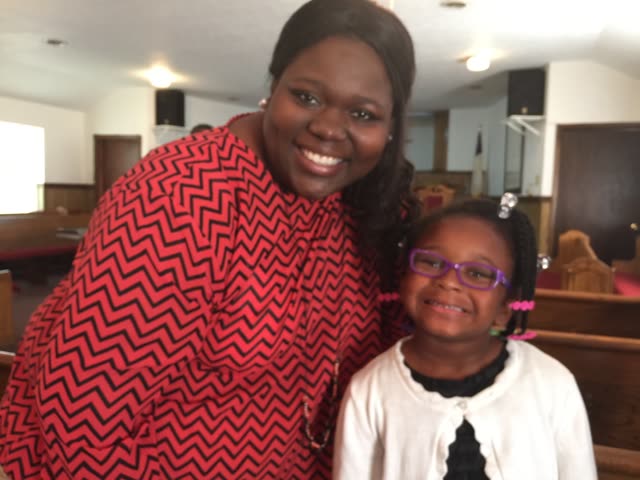 A woman in a red dress and a girl in white smile together in the sanctuary.