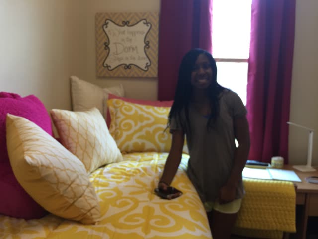 A woman stands beside a bed with decorative pillows.
