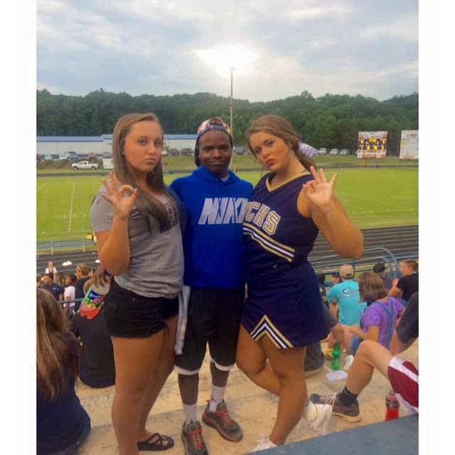 Three young athletes in uniforms stand on a sports field.