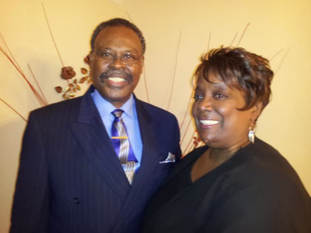 A man in a suit and tie and a woman in black pose together.